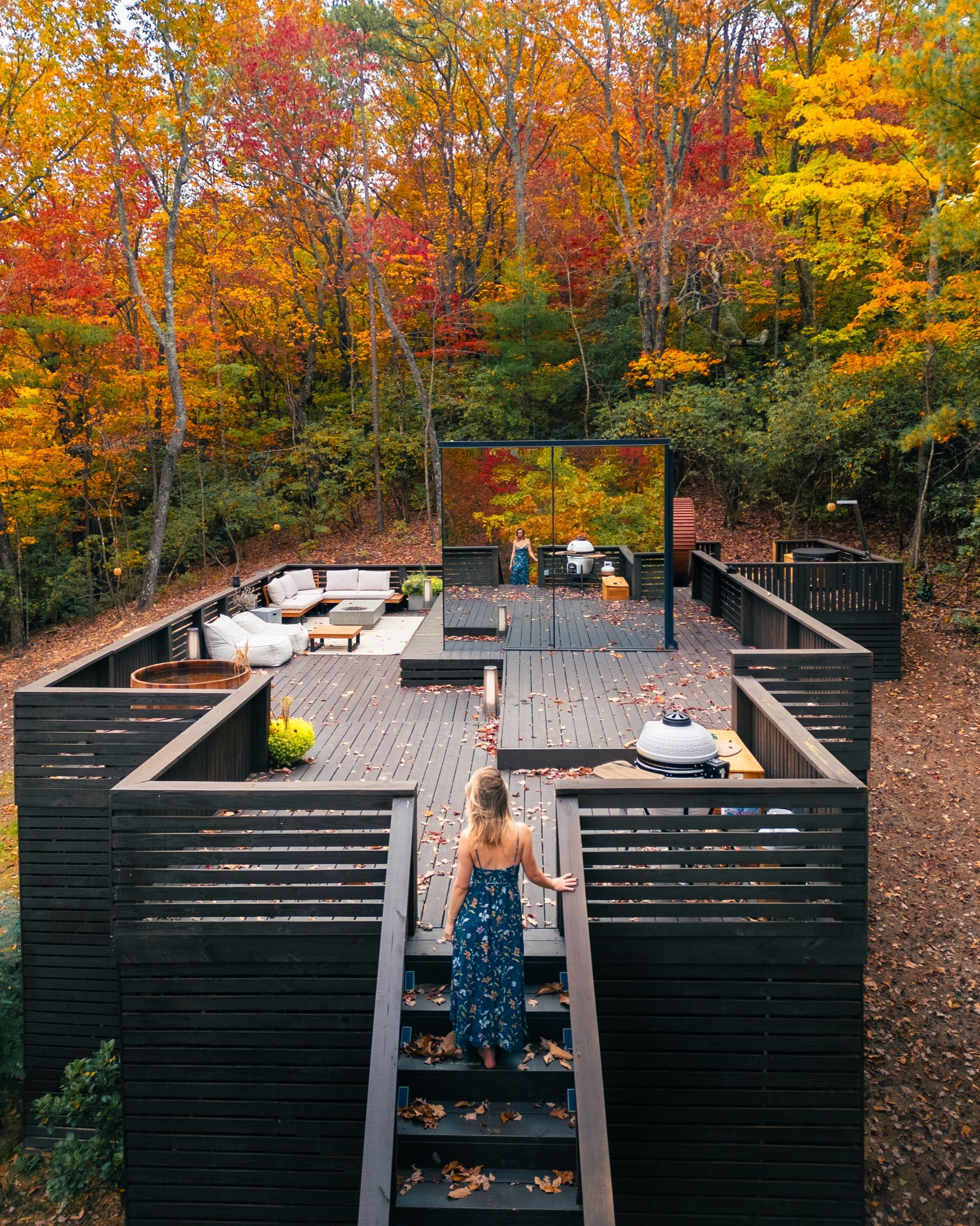 Woman walking up stairs to a large dark wooden deck in autumn forest