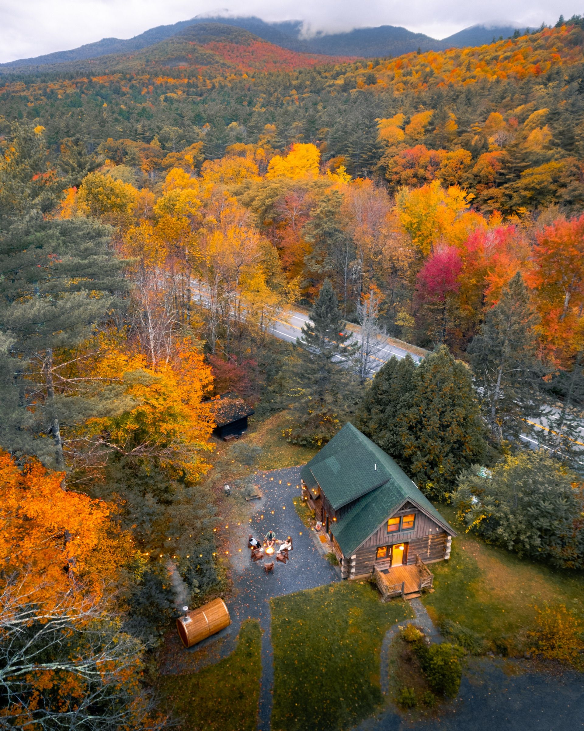 Aerial view of a log cabin and campfire circle among autumn forest
