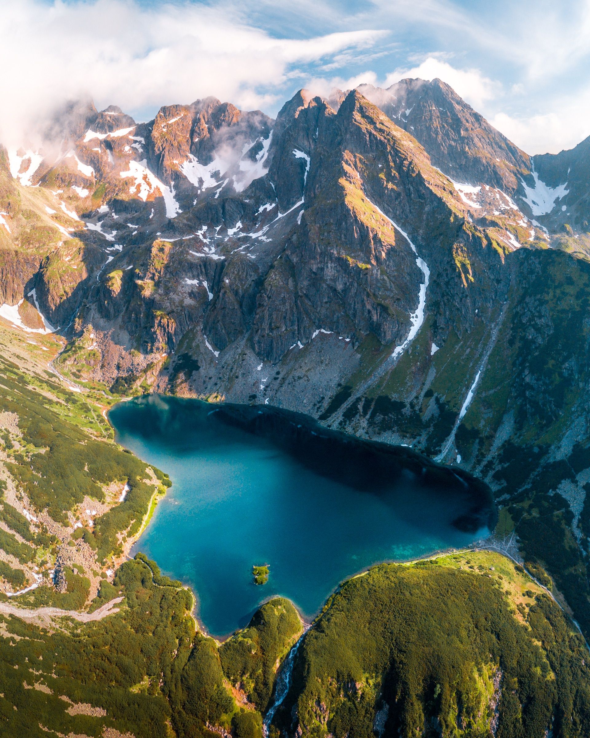 Aerial view of a deep blue lake below jagged, snow-streaked peaks