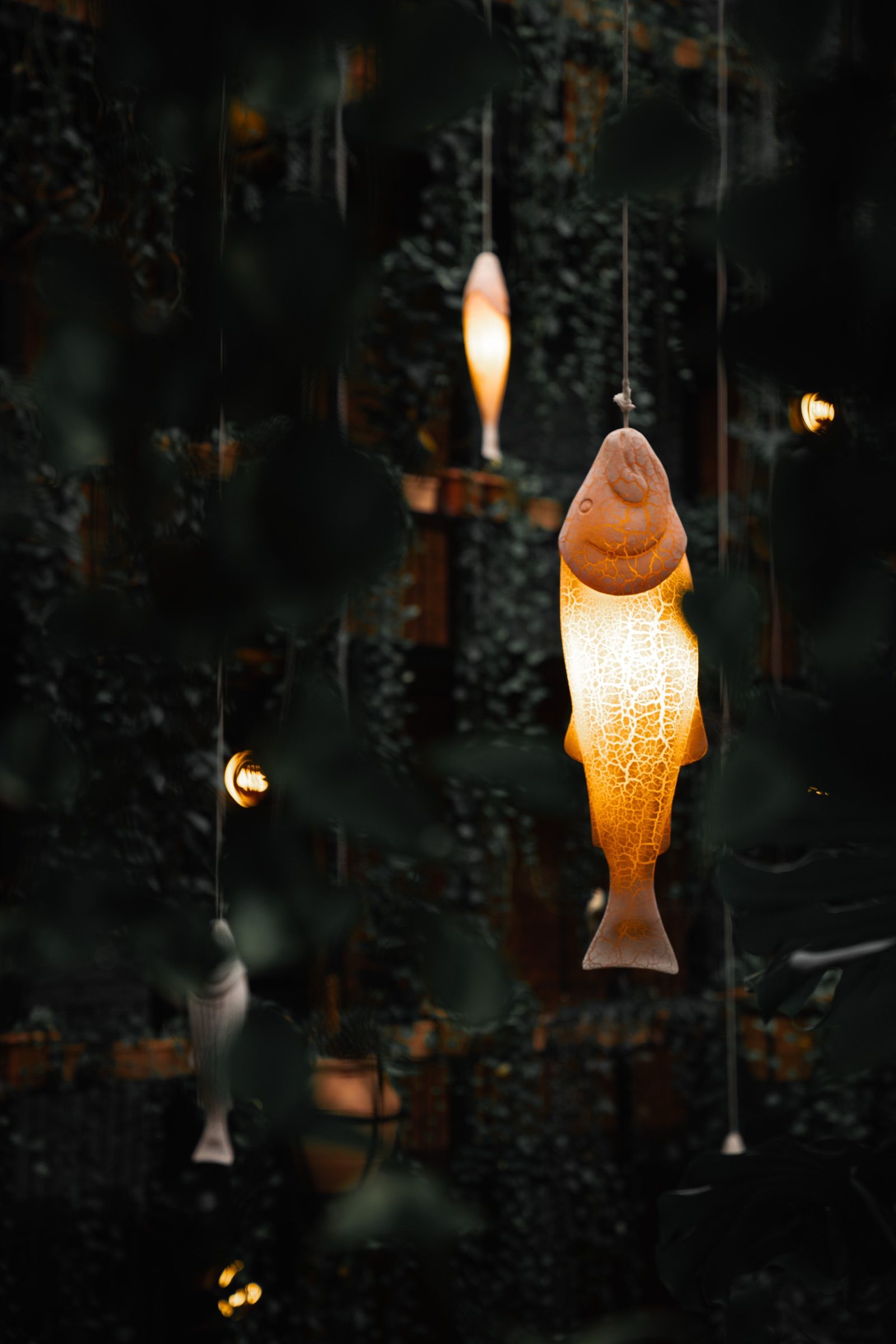 Glowing fish-shaped lanterns hanging among dark foliage