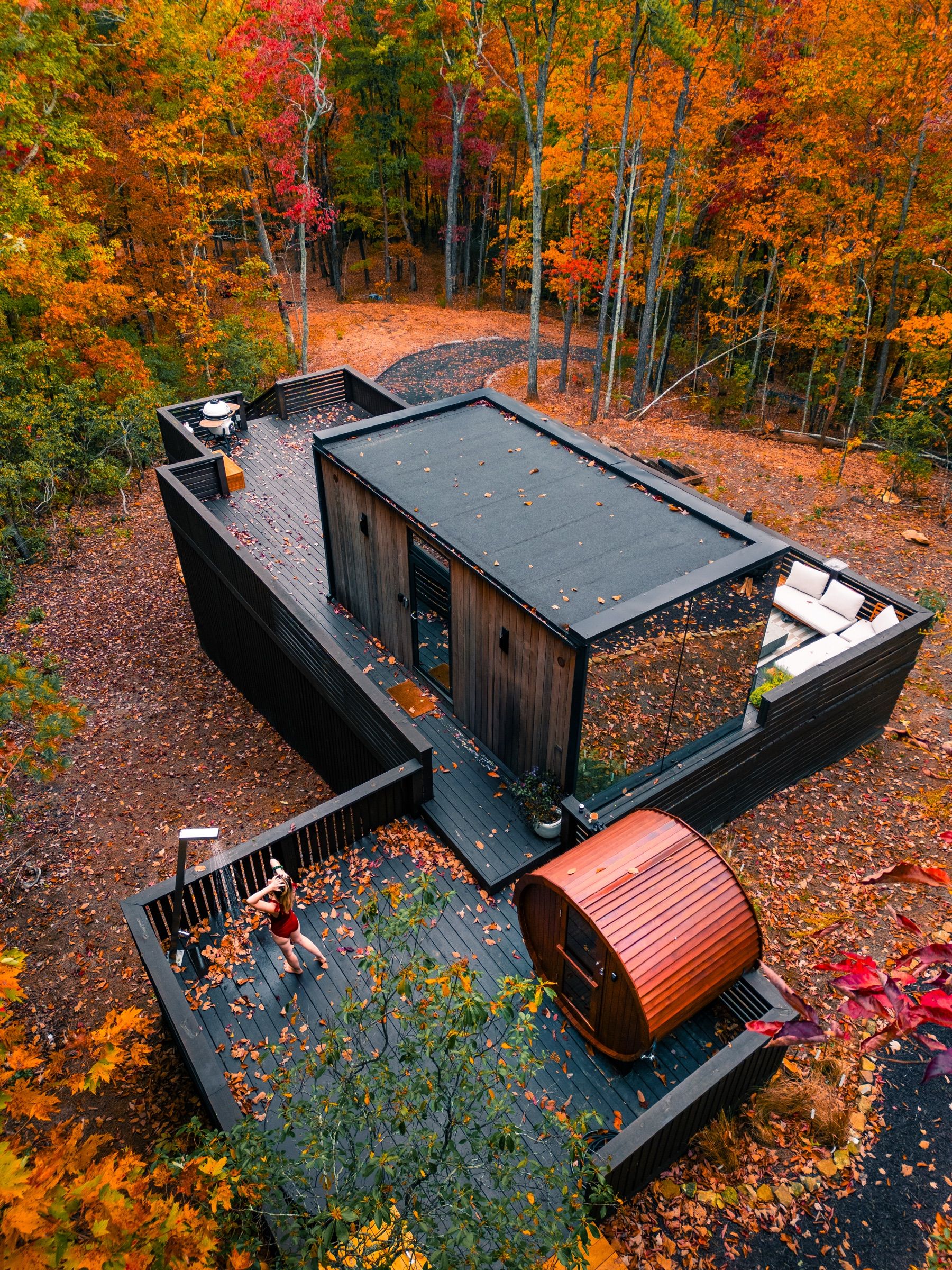Aerial view of a dark modern cabin, deck and barrel sauna among fall leaves