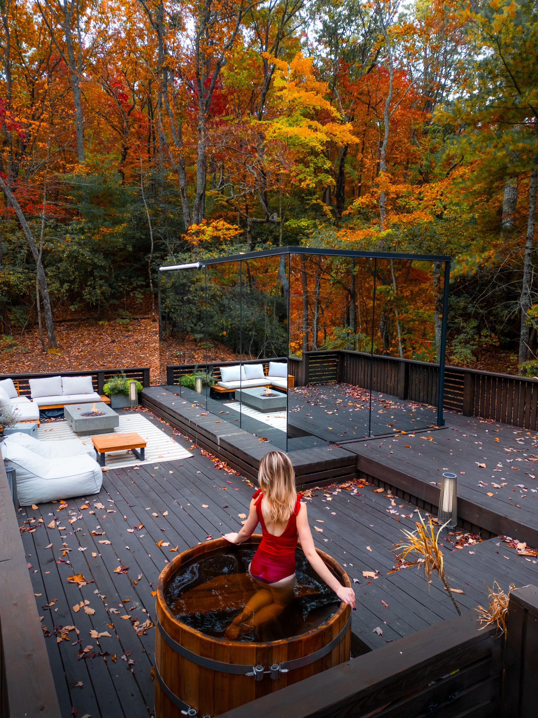 Woman in a red swimsuit in a wooden cold plunge tub on a deck in autumn woods