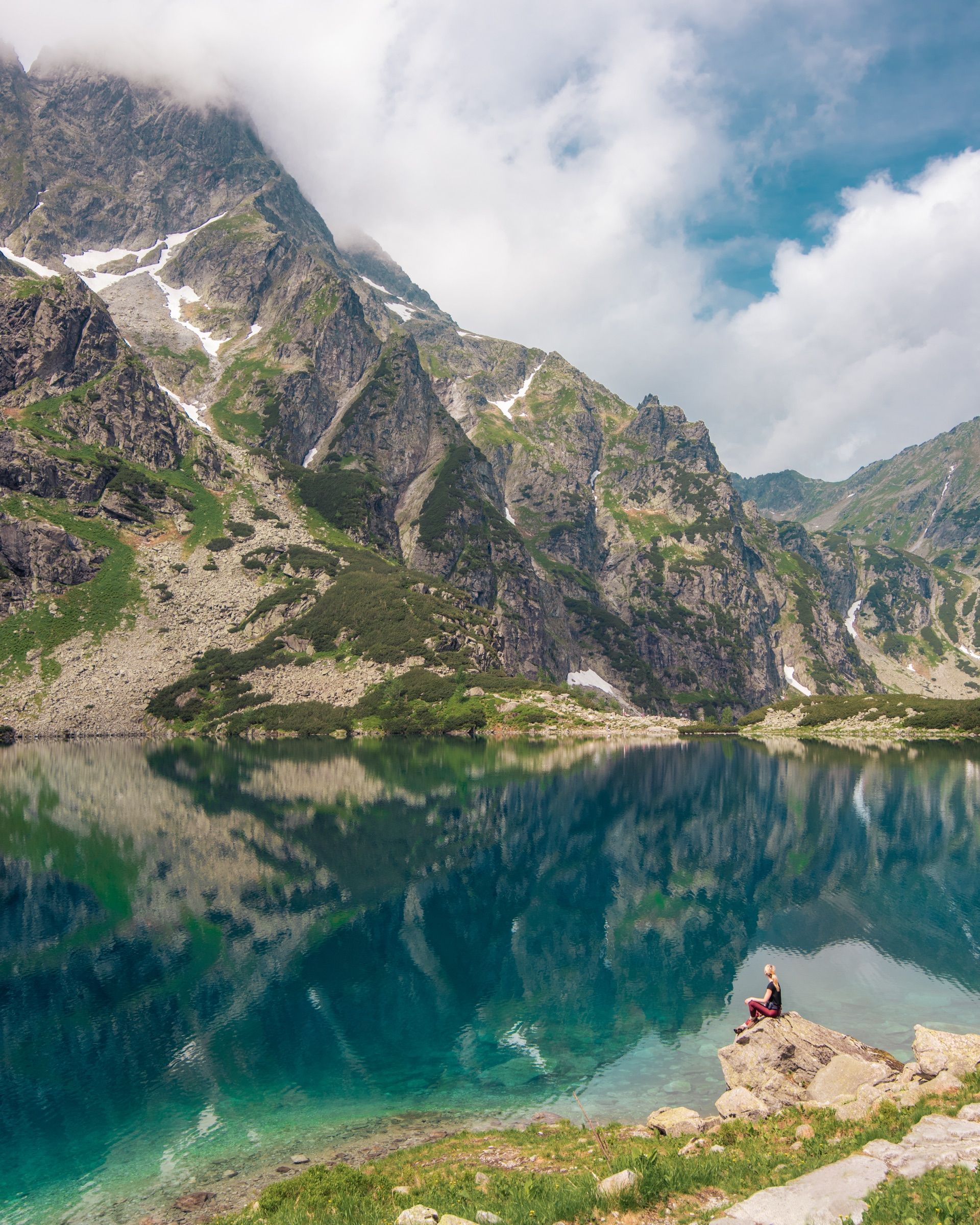 Hiker sitting on a rock beside a still lake reflecting rocky mountains