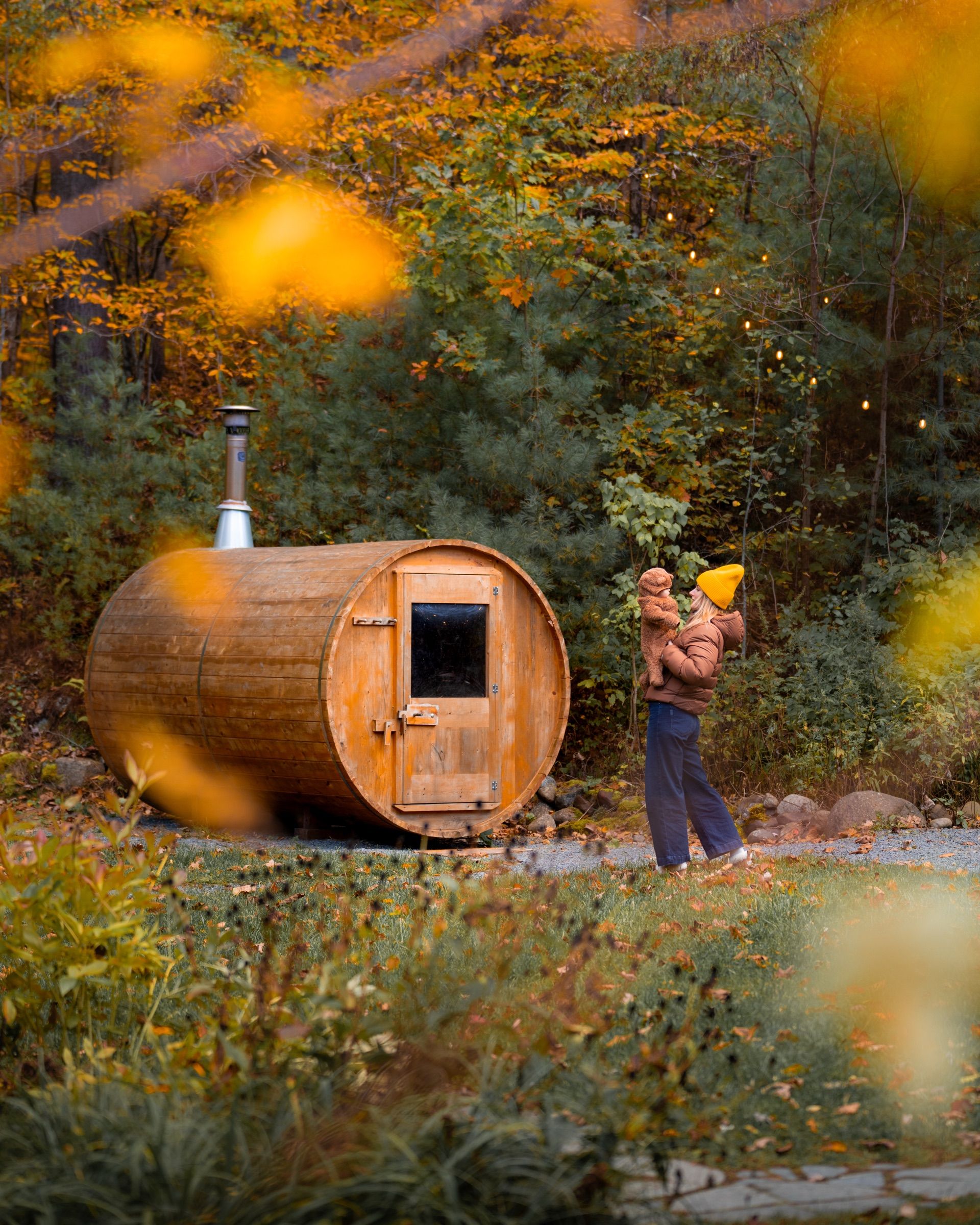 Woman holding a small child beside a barrel sauna in autumn woods