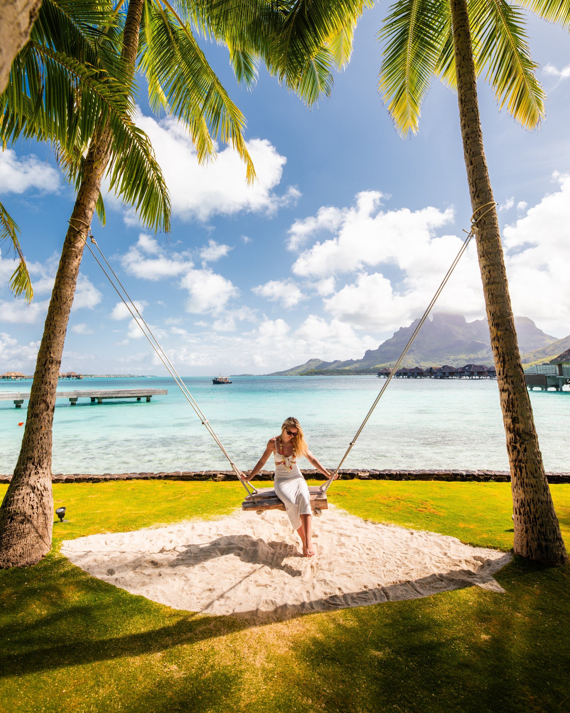A woman in white on a rope swing between palm trees above the Bora Bora lagoon