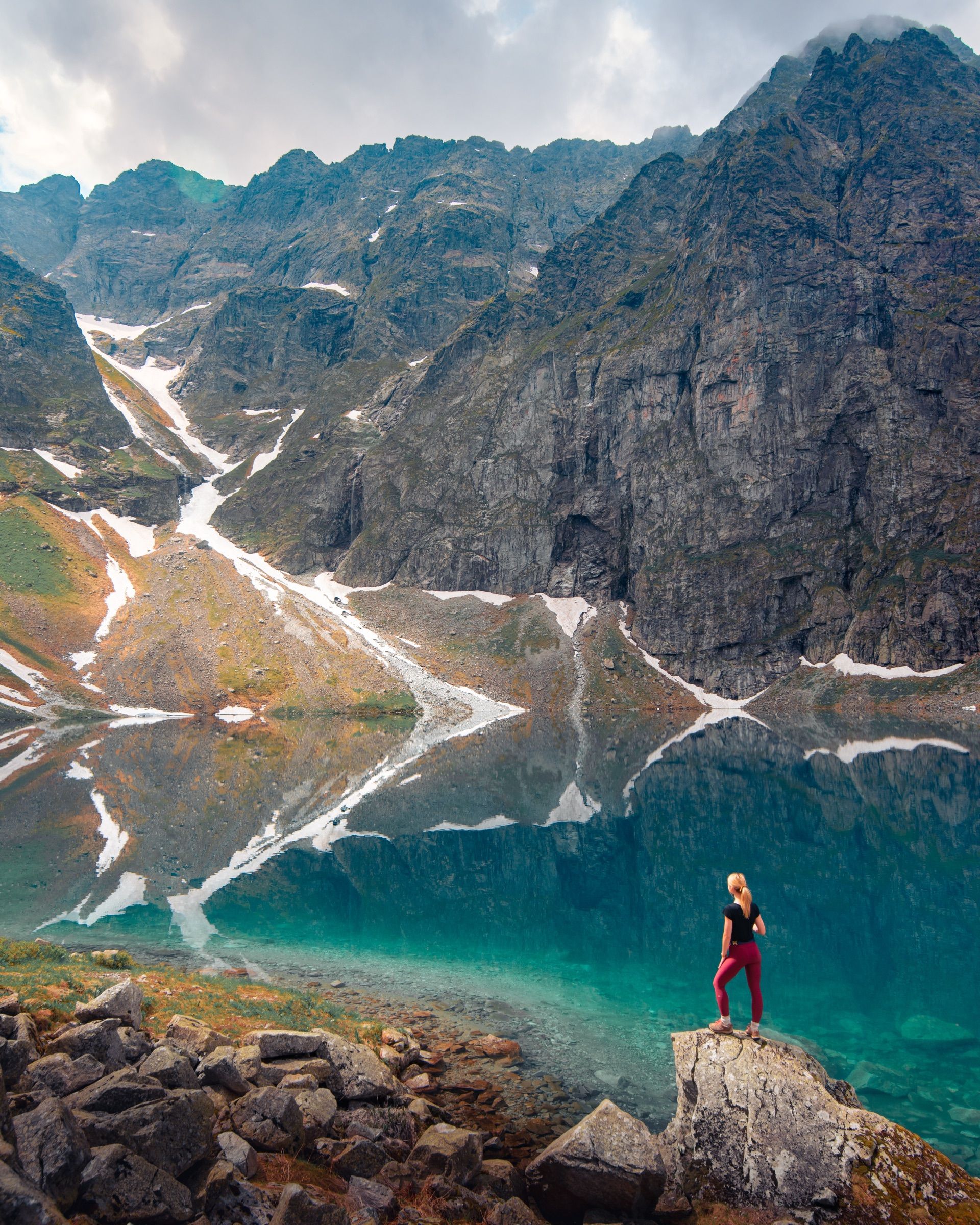 Hiker standing on a boulder at the edge of a turquoise lake below steep cliffs