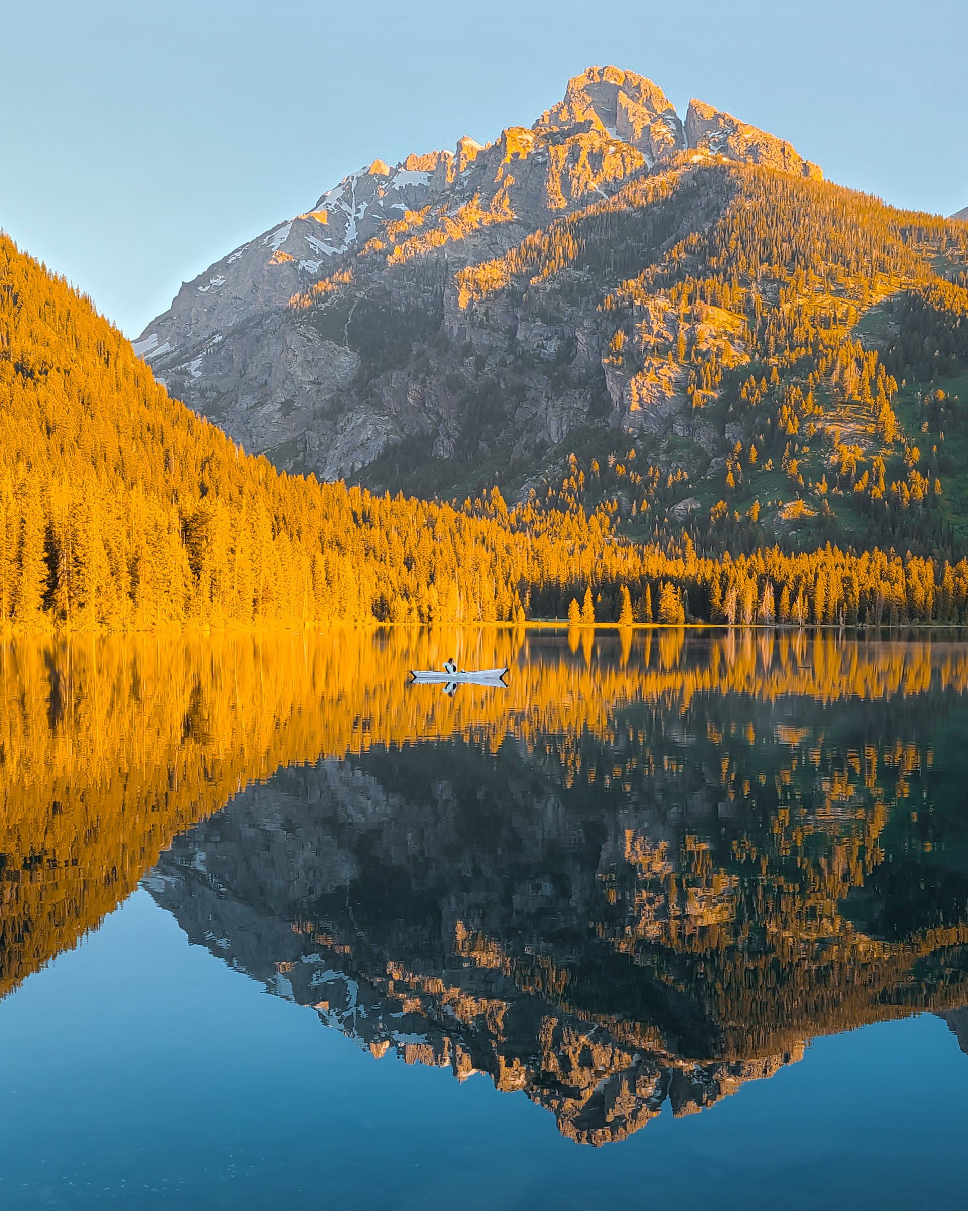 A lone kayak on a mirror-still lake reflecting a golden-lit granite peak and forest