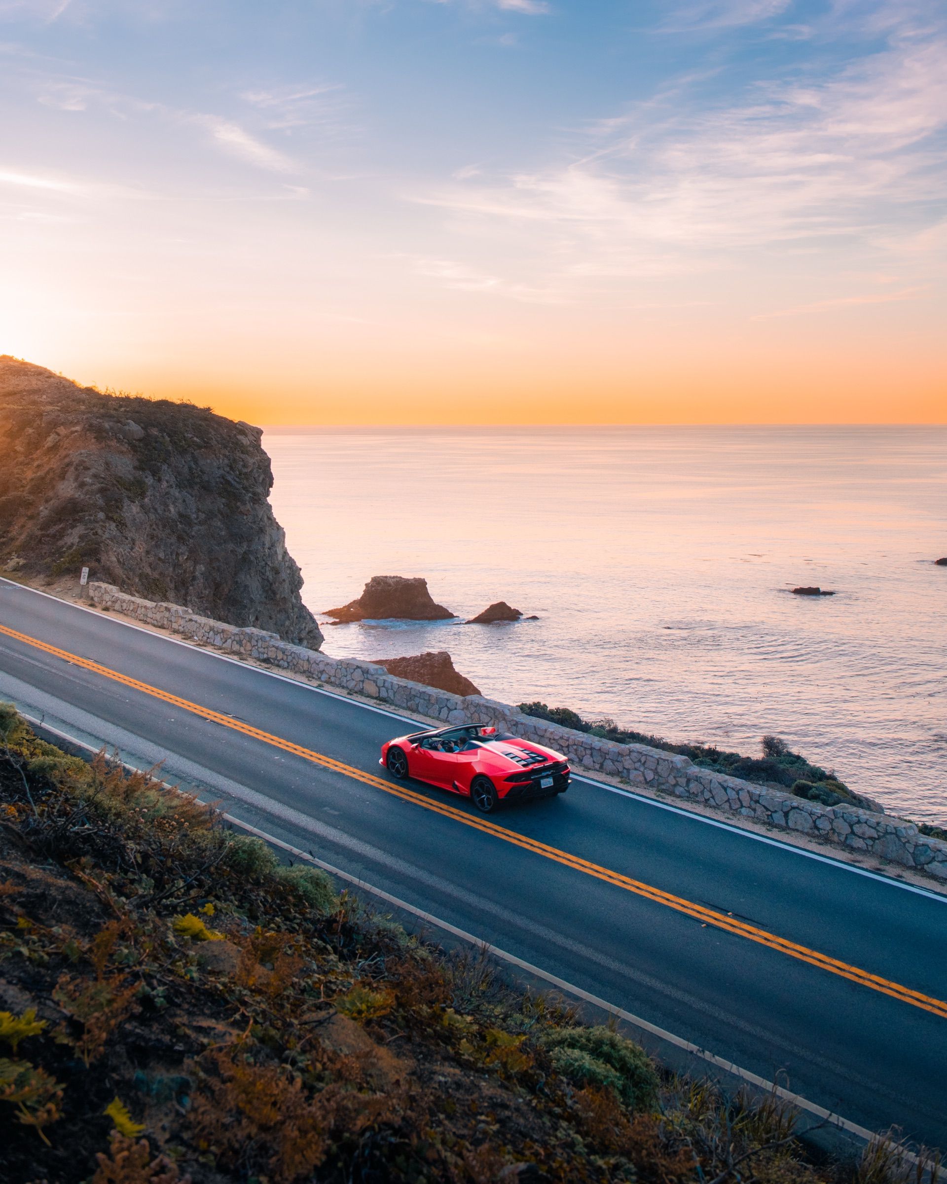 Red Lamborghini driving a coastal highway above the Pacific at sunset, Big Sur