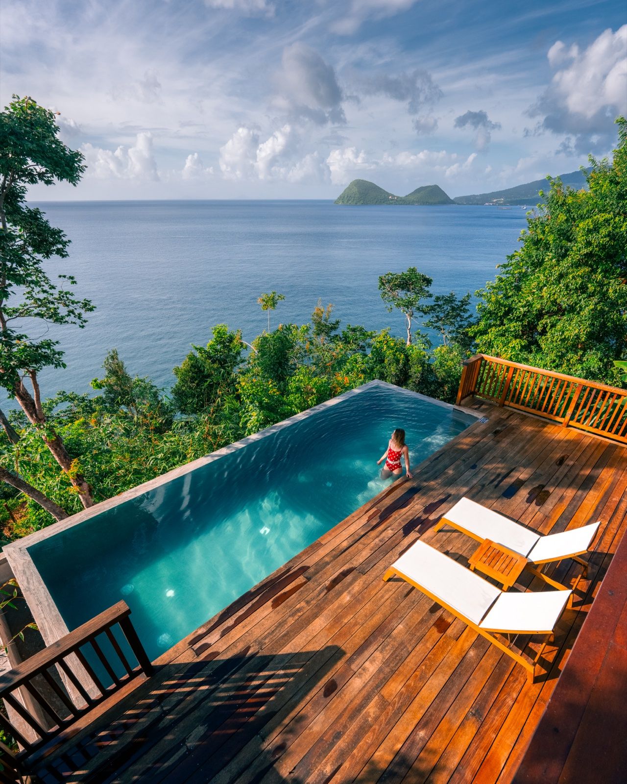 Woman in a cliffside infinity plunge pool on a wooden deck above the sea