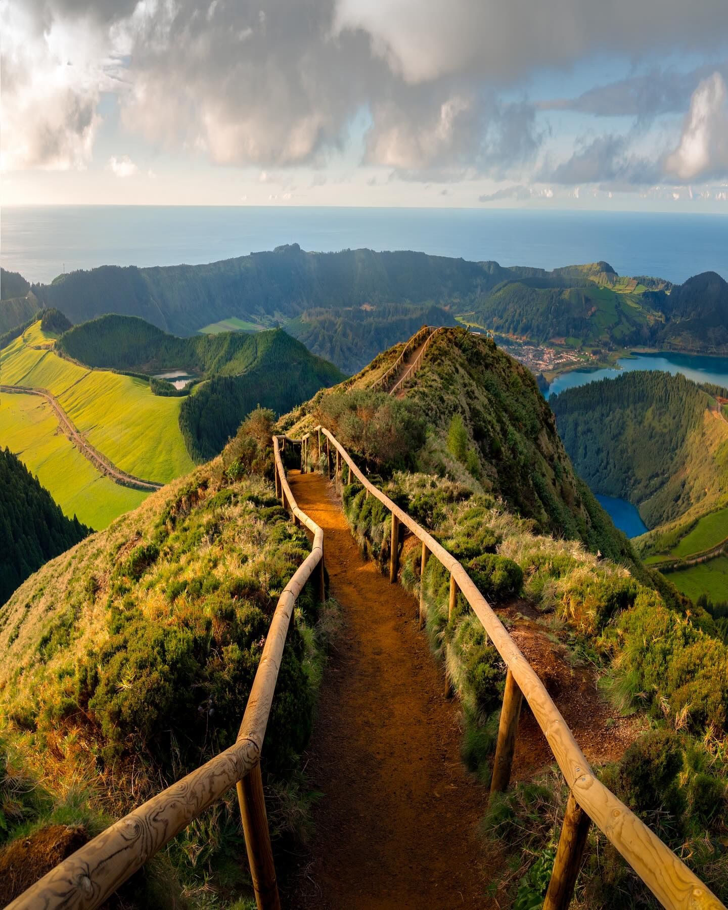 A railed dirt trail along a narrow ridge toward crater lakes and the ocean