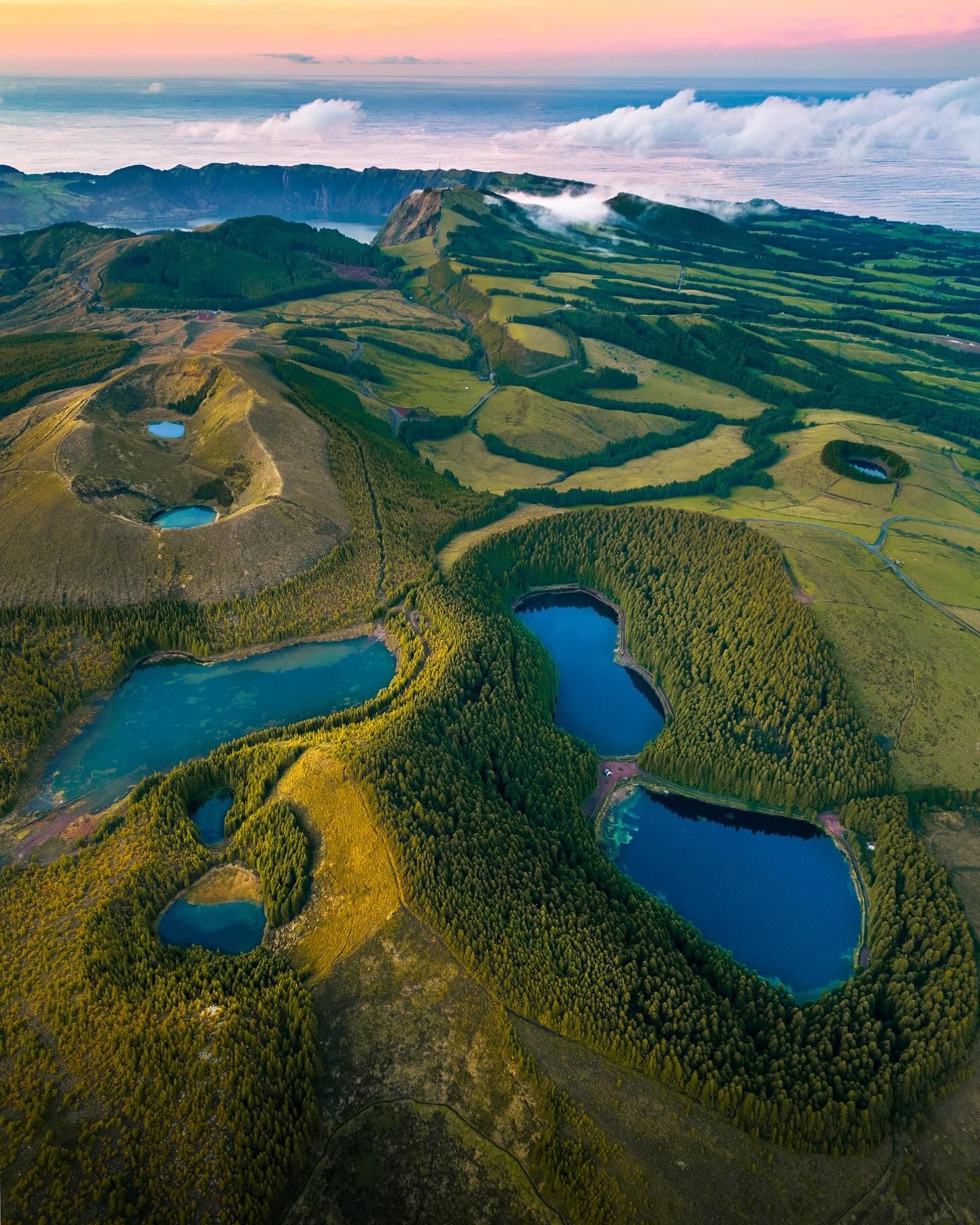Aerial of several blue crater lakes among forested volcanic hills on São Miguel