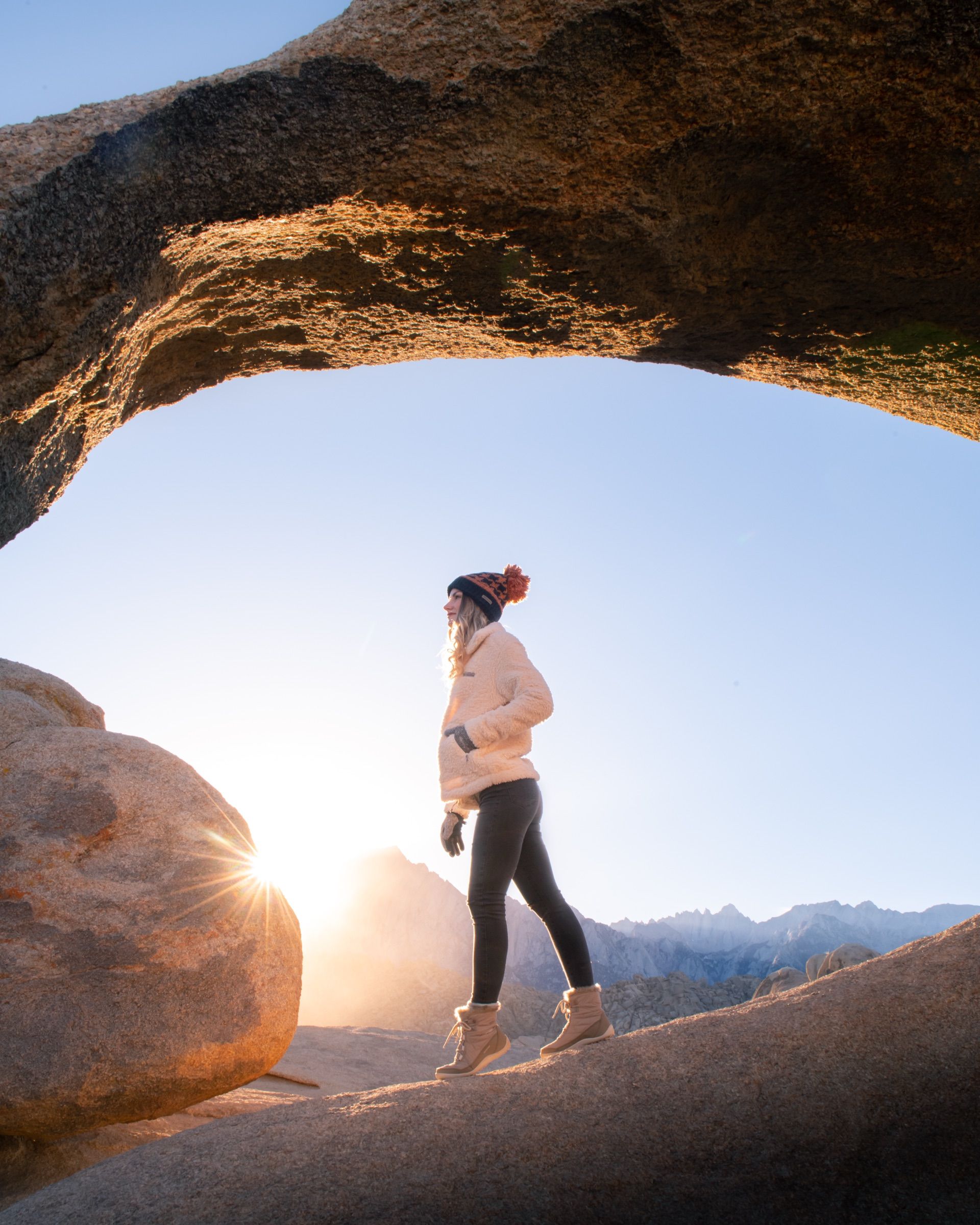 Woman in a cream fleece standing under a granite arch at sunrise