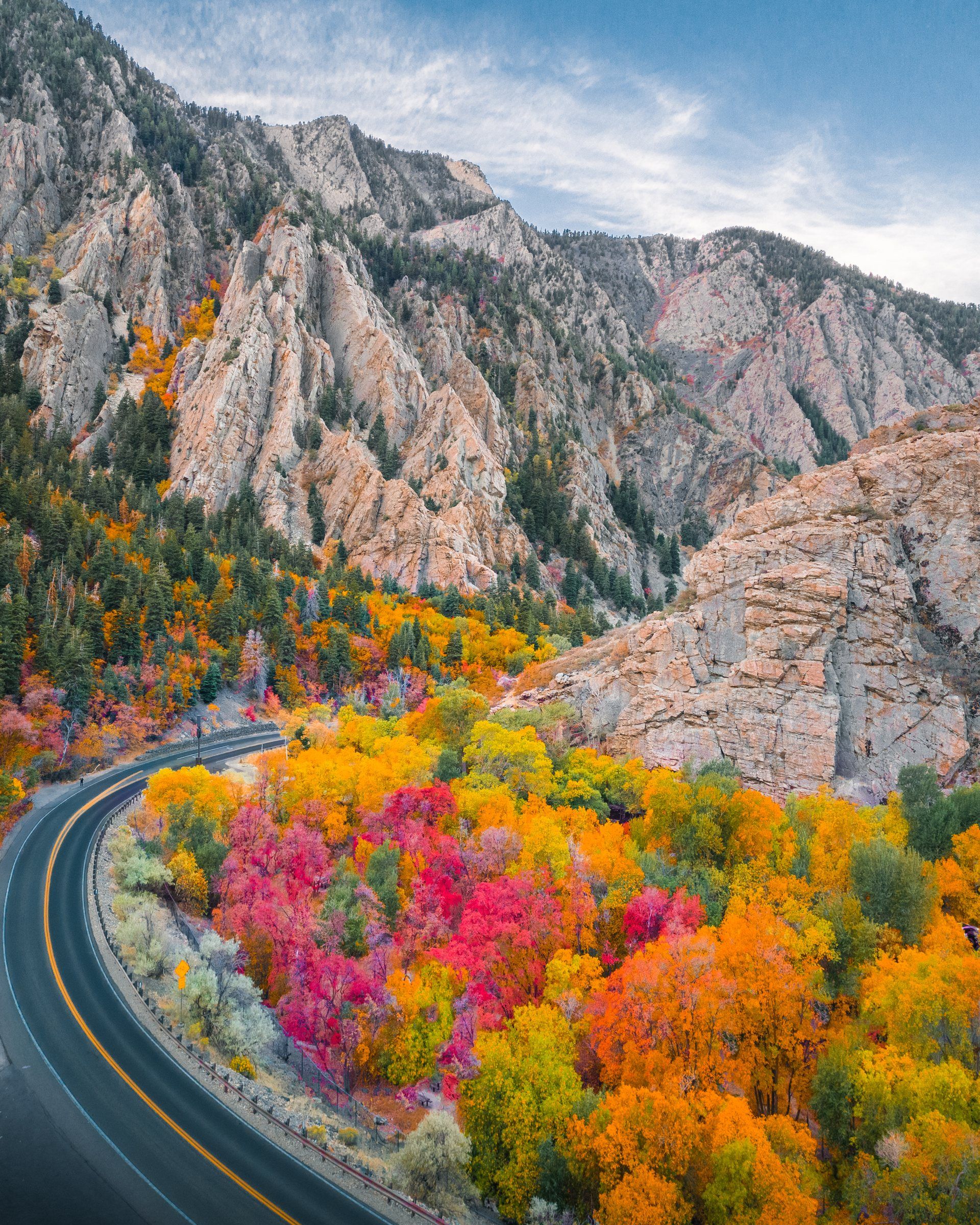 A curving canyon road through bright autumn foliage below pale limestone cliffs