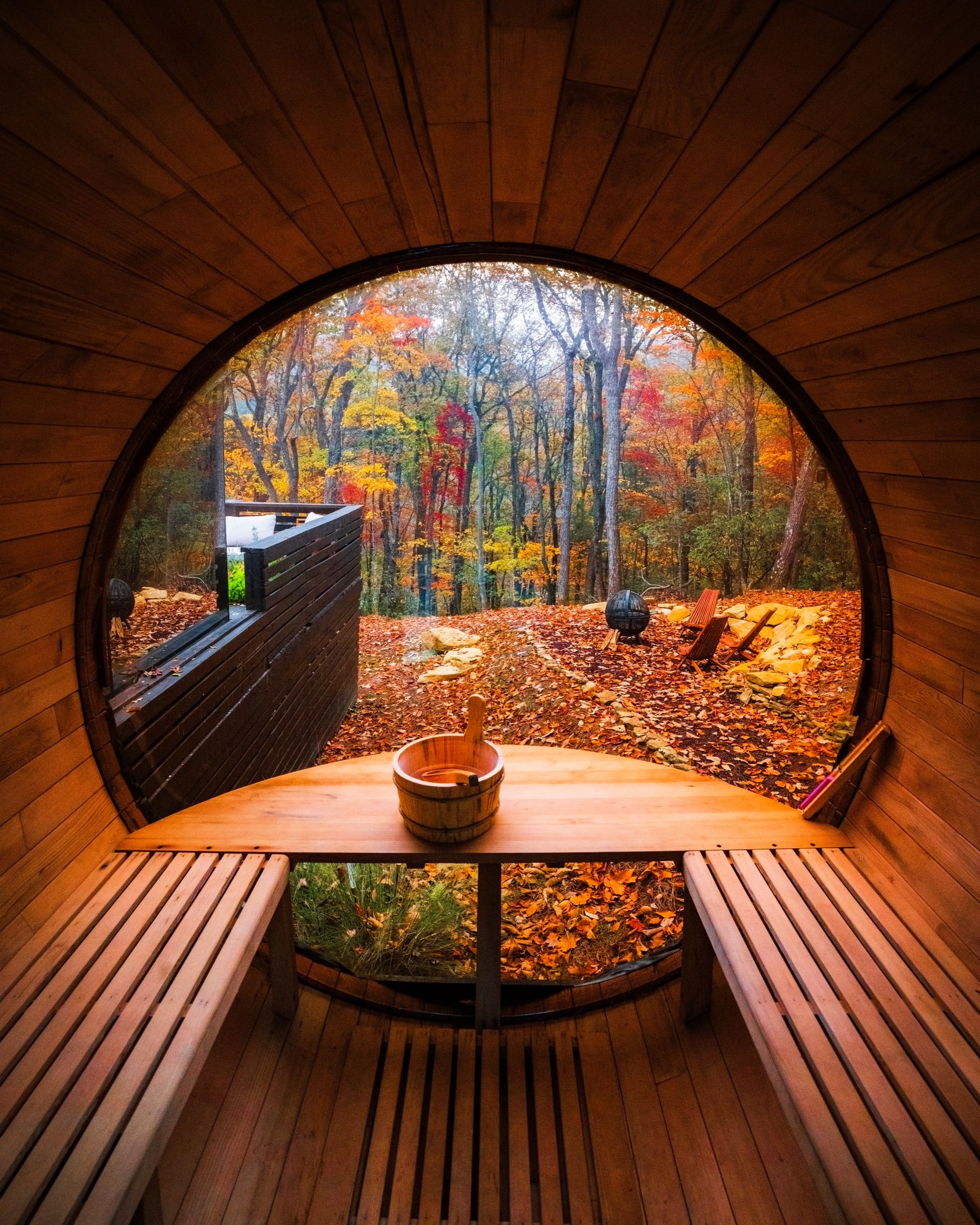 View from inside a barrel sauna through a round window to autumn trees