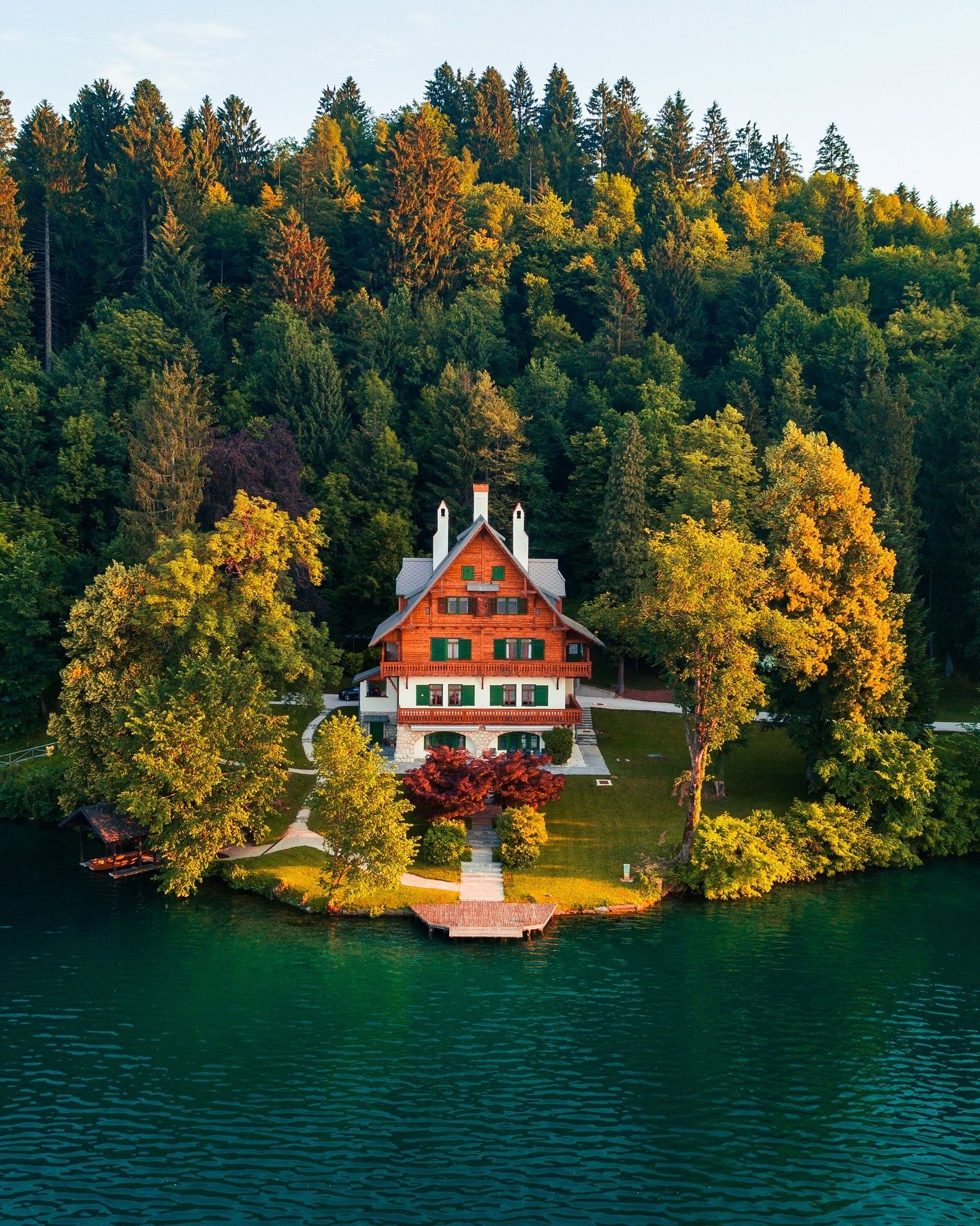 Aerial of a wooden lakeside villa with green shutters on Lake Bled, surrounded by forest