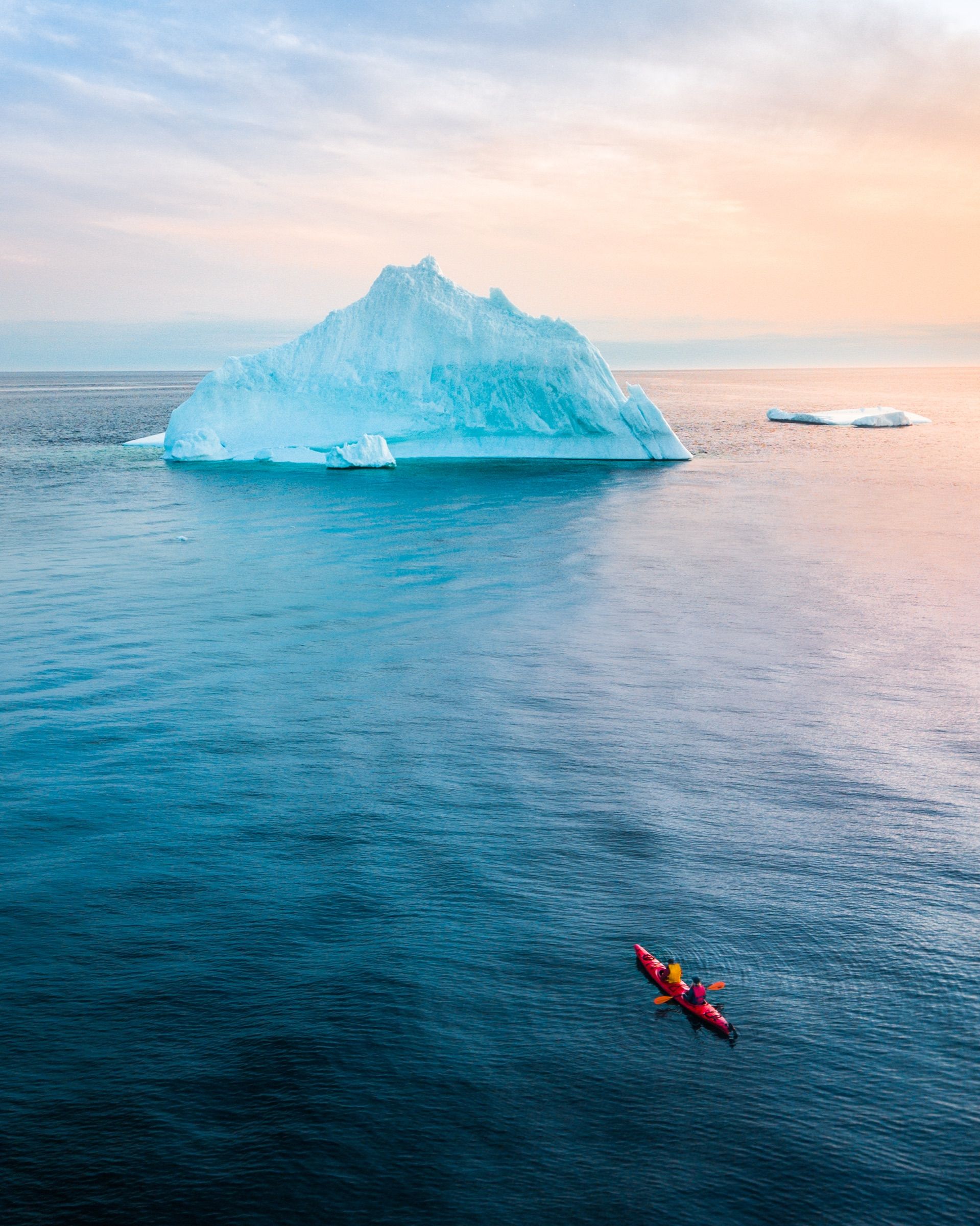 Aerial view of a red kayak paddling toward an iceberg at dusk