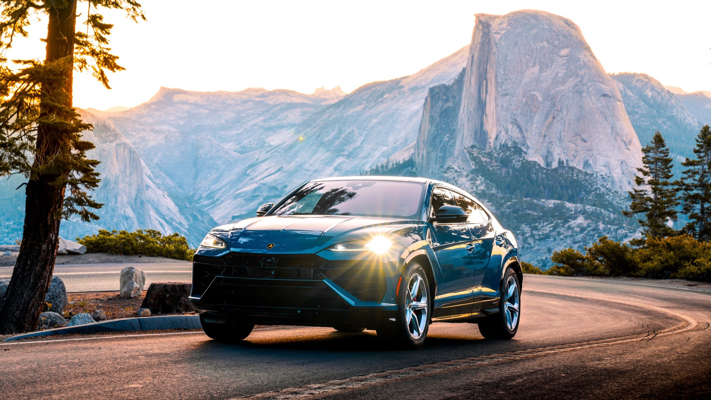 Blue Lamborghini Urus with headlights on, on a curving road below Half Dome, Yosemite
