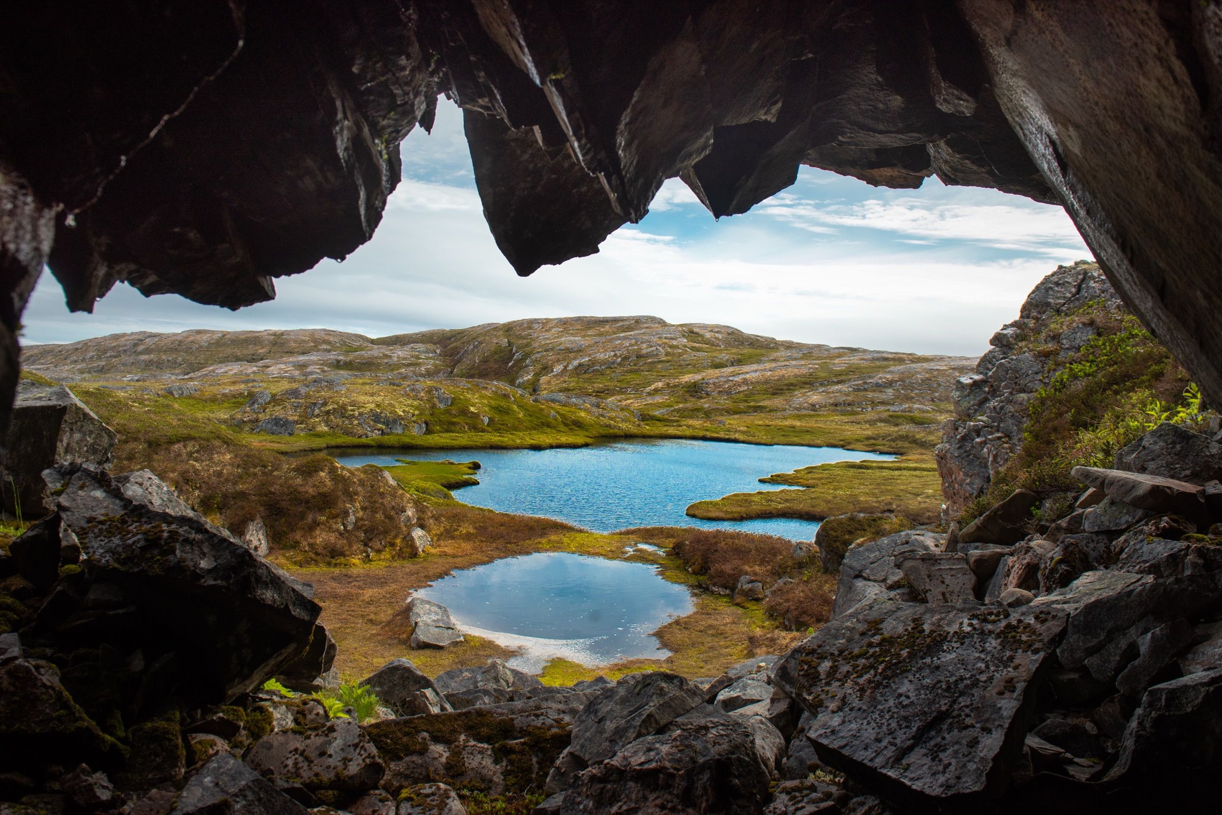 View from inside a rock cave over green barrens and small ponds