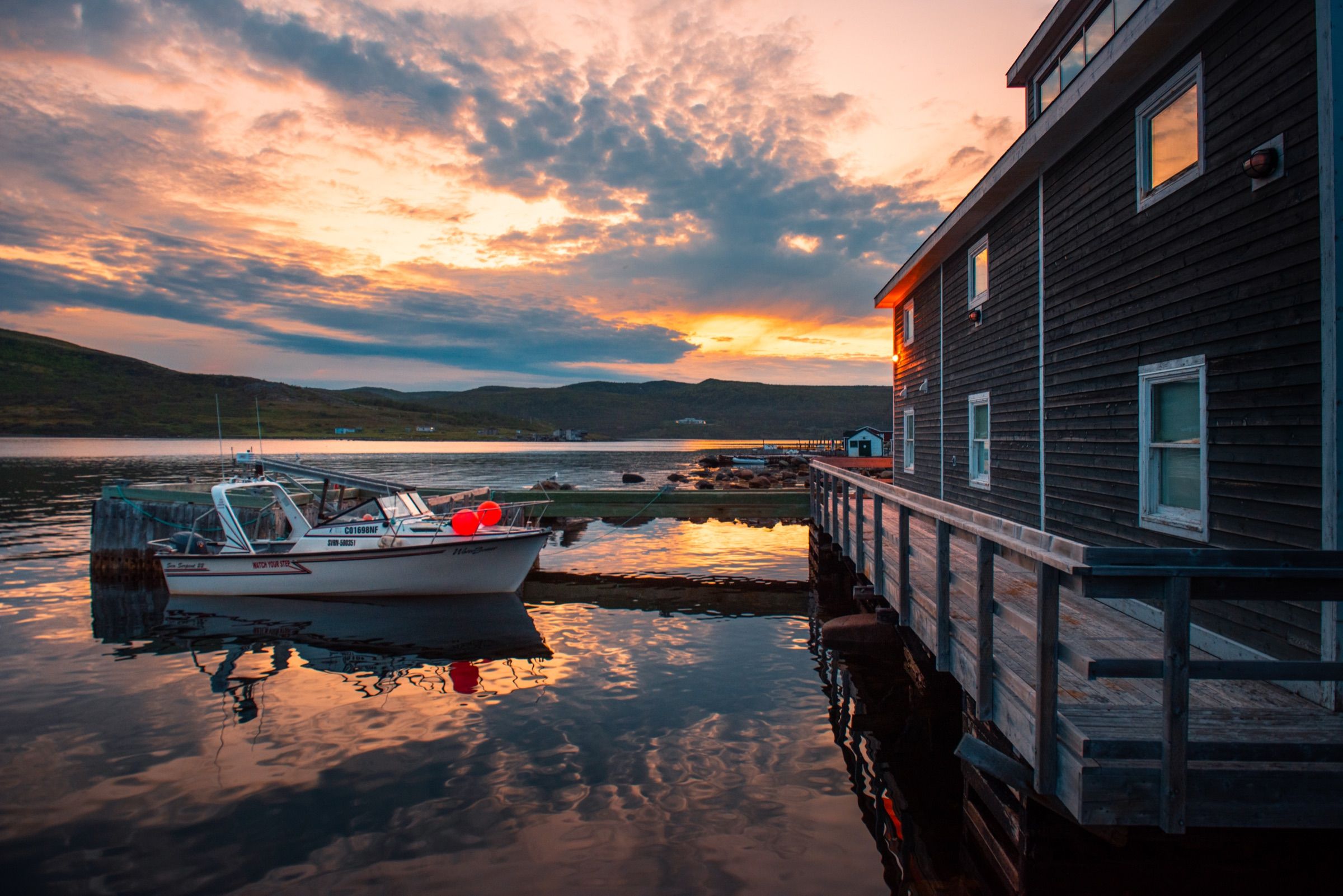 Fishing boat moored beside a wooden waterfront house at sunset