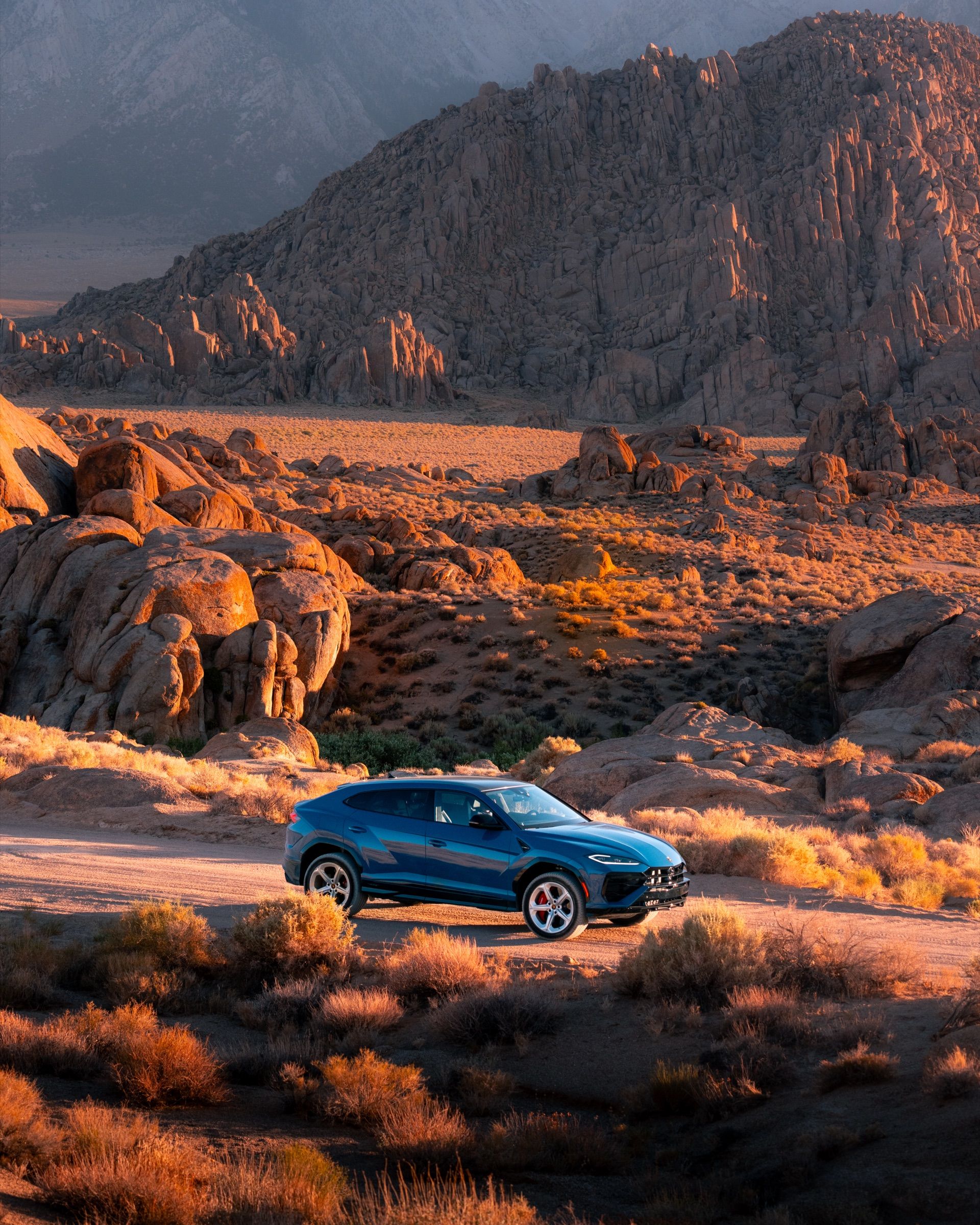 Blue Lamborghini Urus parked among sunlit boulders in the Alabama Hills