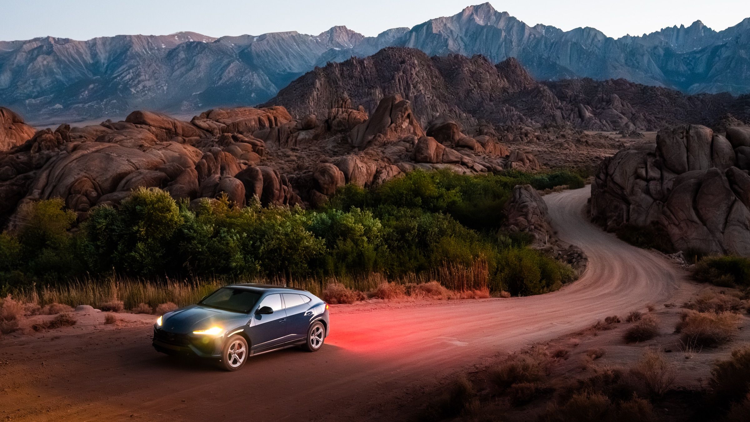 Lamborghini Urus with glowing tail lights on a dirt road through the Alabama Hills below the Sierra Nevada