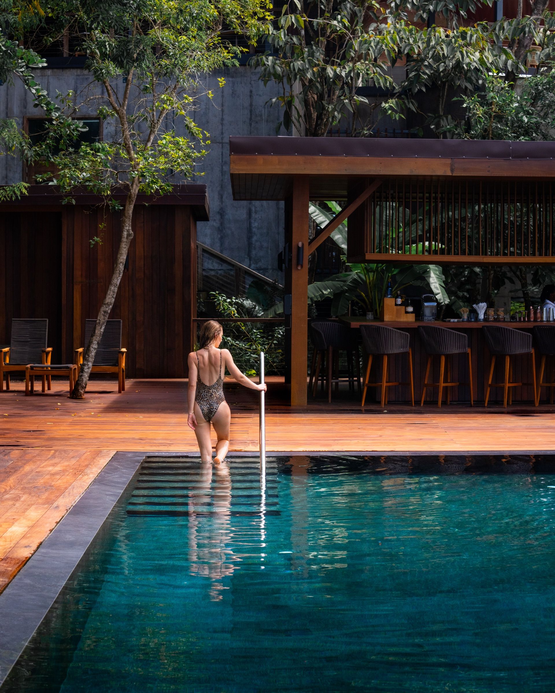 Woman wading into a dark-tiled pool beside an open-air bar