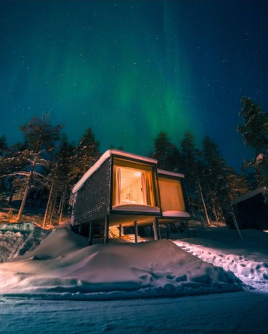 Glowing glass cabin in a snowy forest under the northern lights